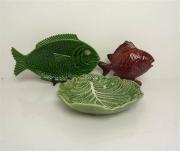 Lote 550 - Lote composto por travessa "peixe" de faiança das Caldas de cor verde, marcada Frutuoso, Caldas da Rainha, com 21x37 cm, mealheiro "peixe" em faiança das Caldas de cor bordeaux, com 20x25 cm e taça "couve" de faiança verde da Fábrica Bordalo Pinheiro, com marcas, com 28x28 cm (com pequena falha no bordo) 