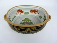 Lote 990 - Centro de mesa de porcelana oriental, decoração em relevo de figuras e flores sobre fundo preto e bege, interior decorado com peixes e nenúfares de tom verde e laranja sobre fundo branco, com marcas, com 14x44x27 cm