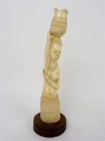 Lote 1025 - Estatueta africana esculpida em marfim com "figura feminina com cesta à cabeça", com base de madeira exótica, com 28 cm de altura