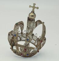 Lote 321 - Coroa para imagem religiosa em filigrana de metal dourado, com aplicação de pequenas pedras multicores, encimada por cruz e bola. Dimensão: 16x10ø cm. Sinais de uso, elemento solto.