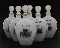 Lote 5244 - COLECÇÃO DE GARRAFAS EM PORCELANA - Composto por 6 garrafas, decoradas com carros antigos e inscrições Whisky, Cognac, Porto, Licor, entre outros, com filetes dourados. Dim: 24 cm de altura. Nota: sinais de uso, vidrado com craquelé