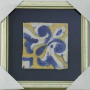 Lote 24 - AZULEJO SÉCULO XVII - Aplicado em moldura de caixa prateada. Decoração a azul e amarelo. Dim: 14x14 cm (azulejo) e 28x28 cm (moldura). Nota: falhas e defeitos, colado