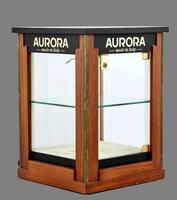 Lote 5474 - VITRINE EXPOSITORA DE MESA - Estrutura em madeira de mogno e metal amarelo, com faces de vidro. Interior com prateleira de vidro e fundo forrado em tecido aveludado. Preparada para electrificação. Cimalhas com publicidade da marca Aurora. Dim: