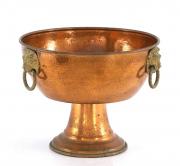 Lote 20 - GRANDE TAÇA EM COBRE MARTELADO - Decoração com 3 pegas em latão com formato de cabeça de leão suportando argolas. Assente em base circular. Dim: 32,5x41 cm (aprox.). Nota: sinais de armazenamento. Falhas e defeitos