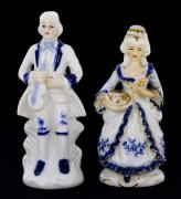 Lote 126 - ESTATUETAS DECORATIVAS EM PORCELANA - Par de figuras ao gosto romântico, em porcelana azul e branca, com ornamentos dourados. Dim: 17 cm de altura. Nota: sinais de uso