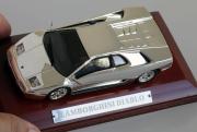 Lote 20 - MINIATURA AUTOMÓVEL CLÁSSICA - “Lamborghini Diablo” com um original banho de cor prata ou ouro ou misto, esta coleção é muito interessante e original. Os modelos estão assentes numa plataforma de madeira envernizada e protegidos do pó por uma caixa acrílica transparente. Escala 1:43, em muito bom estado, tudo original, sem falhas