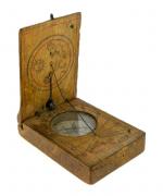Lote 30 - BÚSSOLA - Antiga bussola com relógio de sol em madeira (J. S.). Esta foi das primeiras bussolas construída pelo autor sendo ainda de madeira muito rústica. Dim: 7x5 cm. Nota: desgastes