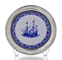 Lote 5363 - PRATO DE SUSPENSÃO EM PORCELANA E PRATA PORTUGUESA 925 - Prato em porcelana da Cerâmica de Conimbriga com decoração a azul com caravela. Aba em prata com decoração lisa. Peso da prata: 75 g (aprox). Dim: 32 cm. Nota: com marcas de contraste em