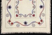 Lote 24 - TOALHA DE LINHO COM BORDADO DE VIANA - Toalha de mesa em tecido de linho bege, com bordado de Viana em linha azul, vermelho e preto, com remate de franjas. Dim: 115x115 cm. Nota: sem uso