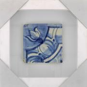 Lote 87 - AZULEJO, SÉC. XVIII - Azulejo antigo aplicado em moldura vitrine (branca). Decoração em tons de azul com motivos vegetalistas. Dim: 14x14 cm (azulejo), 29,5x29,5 cm (moldura). Nota: sinais de manuseamento