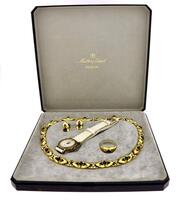 Lote 189 - MATHEY TISSOT, CONJUNTO DE RELÓGIO DE PULSO E ADEREÇO DE SENHORA - Relógio com caixa em metal dourado com 24 mm e bracelete em pele. Movimento de quartzo e mostrador com numeração romana e marcadores. Adereço composto de colar, par de brincos e