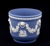 Lote 53 - WEDGWOOD, FLOREIRA EM PORCELANA INGLESA - Floreira marcada na base, Made in England, Jasper Ware, porcelana em azul claro com decoração clássica e grinaldas de parras e uvas relevadas a branco. Em bom estado. Dim: 12 cm de altura