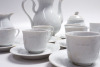 Lote 11 - SERVIÇO DE CAFÉ EM PORCELANA - serviço de café em porcelana da marca Quinta Nova, decoração Classic Branco ornamentado com elementos relevados e com filete dourado, composto por bule, leiteira, açucareiro, 12 chávenas com respetivos pires, num t - 4