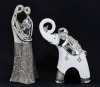 Lote 31 - ELEFANTE E CASAL ROMÂNTICO - Conjunto de 2 peças decorativas em faiança, composto por elefante e casal romântico, decoração relevada em tom prateado e branco. Dim: 30 cm (casal)