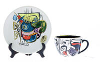 Lote 217 - SONJA BRZAK STUDIO - Conjunto de chávena e prato em cerâmica, Colecção "Enigma - Cups & Saucers", desenho DORA, decoração policromada. Dim: 18,5 cm (prato). Com selo e Certificado de autenticidade. Nota: pintora e ceramista, Sonja Brzak, vive e