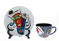 Lote 304 - SONJA BRZAK STUDIO - Conjunto de chávena e prato em cerâmica, Colecção "Enigma - Cups & Saucers", desenho VERA, decoração policromada. Dim: 18,5 cm (prato). Com selo e Certificado de autenticidade. Nota: pintora e ceramista, Sonja Brzak, vive e