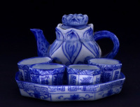 Lote 131 - CONJUNTO DE SAKÉ EM PORCELANA ORIENTAL ANTIGO - Porcelana vidrada pintada á mão em azul sobre fundo branco. Decoração com figuras de fénix, folhas de lótus, elementos vegetalistas e caracteres. Composto de bule, 4 copos e prato em formato octog