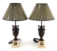 Lote 220 - CANDEEIROS DE MESA - Par de candeeiros em resina em forma de vasos clássico sobre pedestais simulando marfim e ébano. Abat-jours em tela mesclada de negro e dourado. Dim: 52 cm