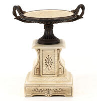 Lote 391 - TAÇA COM PEDESTAL - Taça em resina branca e negra simulando marfim e ébano com decoração gravada e 2 asas assente em base de resina simulando marfim com decoração gravada. Dim: 24x20x16 cm