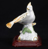 Lote 102 - PÁSSARO - Escultura em porcelana com decoração policromada e dourados, assente em base de madeira, representando "Pássaro". Dim: 10 cm (altura)