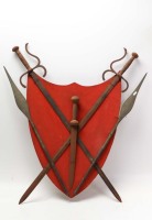 Lote 153 - PANÓPLIA - panóplia com espadas e lanças em ferro sobre brasão vermelho. Dimensão: c. 92x88 cm. Marcas, oxidação