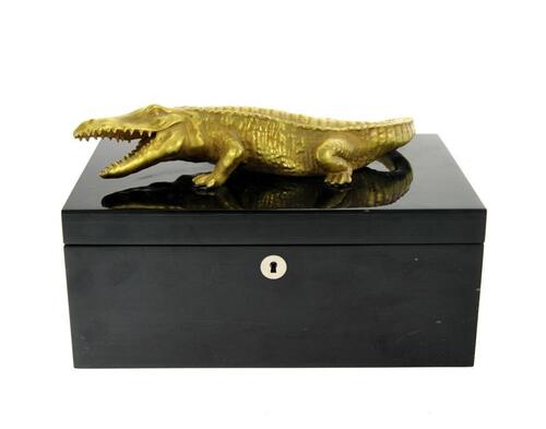 Lote 13 - VILLARI, CAIXA GUARDA-JÓIAS - Made in Italy, modelo Crocodilo, em madeira lacada a negro, tampa decorada com crocodilo em porcelana dourada. Interior forrado e compartimentado. Caixa similar à venda por € 2.304. Dim: 16x30x20 cm. Nota. sinais de