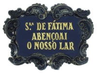 Lote 79 - MOLDURA - Moldura com decoração repuxada e cinzelada de volutas e concheados com placa em vidro negro e inscrições a dourado "N.S. de Fátima Abençoai Este Lar". Dim: 17x21 cm. Pequenas amolgadelas.