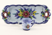 Lote 65 - CONJUNTO EM FAIANÇA DE ALCOBAÇA - Composto de travessa torteira e caneca. Decorações florais policromadas em campo azul. Dim: 16x39 cm (travessa) e 8,5 cm (caneca). Nota: marcadas nas bases