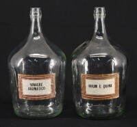 Lote 111 - GARRAFÕES DE VIDRO - Par de garrafões de 5 litros em vidro translúcido, com etiquetas inscritas "Vinagre Aromático" e "Rhum e Quina", vazios. Dim: 35 cm (altura)