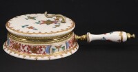 Lote 29 - A.C.F., BEATEIRO EM PORCELANA - Decoração "Índias" policromada pintada à mão, com motivos florais e ornamentos dourados, com pega em latão e porcelana, marcado na base. Dim: 7x25x14 cm