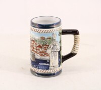 Lote 103 - CANECA DE CERVEJA EM FAIANÇA CROATA - Decoração policromada e relevada com vista de Dubrovnik e figura de Santo. Dim: 14 cm