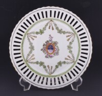 Lote 81 - PRATO DECORATIVO EM PORCELANA - Decoração policromada com brasão e grinaldas de flores, aba vazada e friso dourado, marcado na base. Dim: 25,5 cm. Nota: sinais de uso