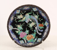 Lote 222 - PRATO EM PORCELANA ORIENTAL - Decoração policromada com pássaro e flores em campo negro. Bordo em palha entrançada. Dim: 25 cm