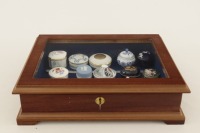 Lote 324 - VITRINE COM COLECÇÃO DE CAIXAS EM PORCELANA - Caixa vitrine em madeira com tampo de vidro. Colecção de 15 caixas em porcelana de diversas marcas como Vista Alegre, Wedgwood, Limoges, Oficina Real, Royal Worcester, Porcelaine de Paris, Limoges, 