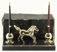 Lote 37 - CONJUNTO DE SECRETÁRIA - Suporte de canetas decorado com cavalo dourado, assente em base de pedra, com par de esferográficas. Dim: 23 cm (comprimento). Nota: pedra com falha e um suporte descolado