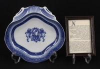 Lote 126 - VISTA ALEGRE, COVILHETE EM PORCELANA - Em forma de concha com decoração a azul comemorativa dos 100 Anos da Wagon Lits em Portugal, marcado na base. Dim: 5x21x21 cm. Nota: junto com texto emoldurado relativo à Wagon Lits e à concepção das peças