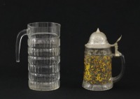 Lote 24 - CANECA DE CERVEJA E JARRO EM VIDRO - Conjunto de caneca de vidro decorada com brasão e tampa de metal e jarro de vidro relevado. Dim: 21 cm (jarro). Nota: sinais de uso