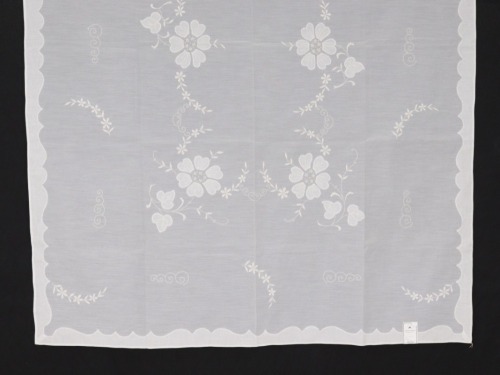 Lote 7 - TOALHA COM BORDADO DA MADEIRA - Toalha de mesa em tecido branco bordado à mão com desenho floral. Com selo de garantia. Etiqueta com pvp de € 239. Dim: 130x180 cm. Nota: sem uso, com etiqueta Isaart. Bordado da Madeira Autorização Nº 19